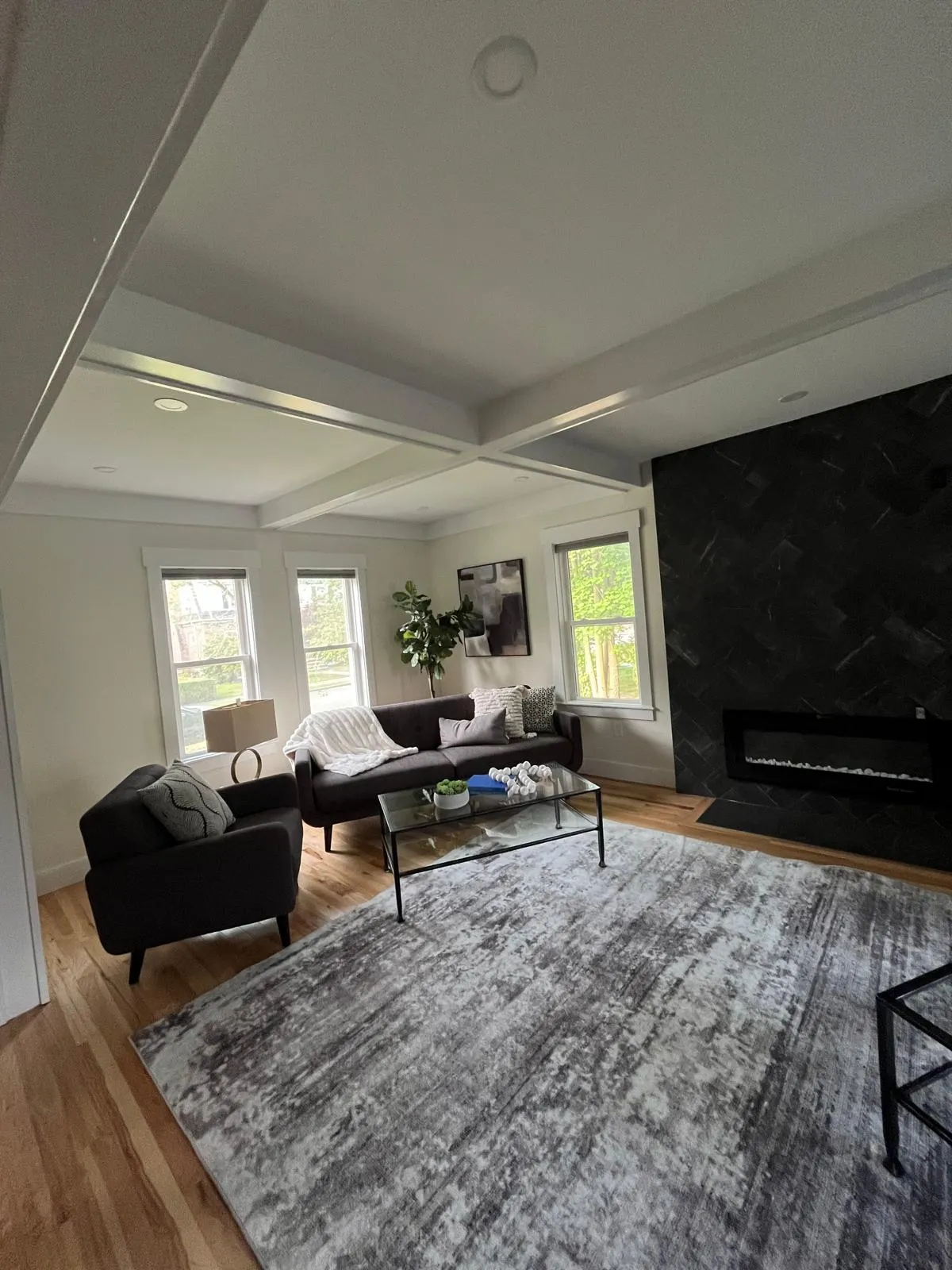 Modern living room with beamed ceiling and dark accent fireplace wall painted by Rainbow Painting Pro in South Shore MA